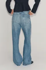 Jeans wide leg de tiro medio confeccionado en denim con efecto lavado, corte relaxed y diseño de pernera ancha. Cuenta con cinco bolsillos, trabillas en la cintura y cierre frontal con cremallera y botón metálico. Presenta aplicación de brillos en toda la prenda.