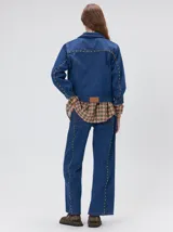Campera denim crop de mezclilla oscura, con apliques metálicos en el pecho, bolsillos delanteros cruzados con detalles bordados y de parches.
