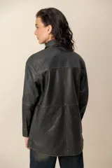 Camisa de cuero negro con efecto lavado, cuello camisero, cierre frontal con broches metálicos y mangas largas.