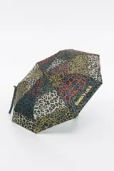 Paraguas plegable con funda de tela estampada en patrón patchwork de leopardo, combinando tonos verde oliva, terracota y negro, con detalles en azul. El mango es de goma color verde oliva con la marca grabada.