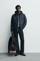 Campera puffer acolchada de corte regular fit en color negro, confeccionada en tejido técnico repelente al agua. Presenta cuello subido con capucha, cierre frontal de cremallera, mangas largas con puños elásticos y bolsillos laterales de vivo.