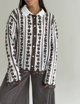 Camisa de manga larga con cuello clásico y cierre frontal de botones. Presenta un diseño de rayas verticales con bordados florales en color marrón sobre fondo blanco, con detalles de encaje en la tapeta central y en el ruedo.