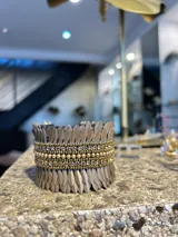 Pulsera tipo brazalete hecho en lentejuelas negras y strass dorados, con base metálica ajustable.