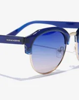 Gafas de sol Hawkers unisex, con montura azul y lentes degradadas de azul a rosa.