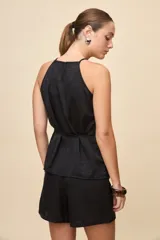 Top negro de calce relajado y textura satinada, con escote halter y lazo fino para ajustar en la cintura.