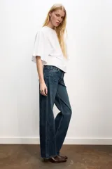 Jeans de mezclilla azul oscuro con efecto lavado, tiro bajo y pierna ancha extra larga. Modelo de cinco bolsillos con cierre frontal de cremallera y botón metálico.