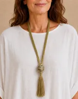 Collar largo color verde pistacho, compuesto por múltiples hilos y un dije esférico de alambre entrelazado con una borla colgante en la parte inferior.