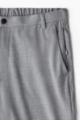 Pantalón de vestir gris claro, de corte slim fit, con bolsillos laterales y traseros. Se ajusta a la cintura con cierre y botón.