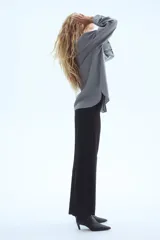 Pantalón negro de vestir, tiro alto, con piernas anchas y corte recto. Presenta pliegues marcados en el frente y cierre frontal oculto.