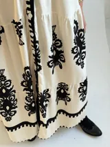 Vestido largo color marfil con estampado ornamental en color negro, escote en V con botones frontales, mangas largas amplias y diseño escalonado en la falda.