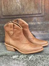 Botas de cuero color suela, de estilo texano, con caña baja, puntera fina y detalles de costuras decorativas.