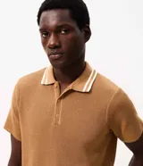 Remera polo marrón de tejido de tricot texturizado, de manga corta, con cuello polo abotonado y detalles de rayas blancas en el cuello.