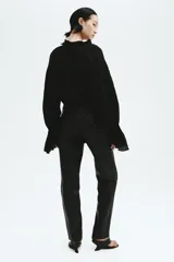 Blusa oversized color negro en tejido liviano de mezcla de lino y viscosa, con cuello elevado plisado y abertura en V con tiras finas. Mangas raglán extralargas con detalles bordados tono sobre tono y puños acampanados con pliegues.