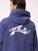 Campera rompevientos Rusty de color azul, con capucha ajustable, cierre frontal completo y bolsillos laterales. Presenta puños elásticos y logo de la marca estampado en el pecho.