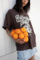 Remera marrón de corte amplio con estampado de texto y dibujo en color blanco.