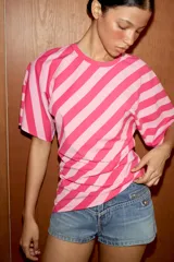 Top de algodón con estampado de rayas diagonales en tonos fucsia y rosado. Presenta cuello redondo, mangas cortas tipo murciélago y un diseño de bajo asimétrico.