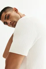 Remera polo de manga corta en punto trenzado suave, color blanco, con cuello abierto y remate acanalado en mangas y bajo.