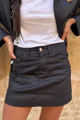 Falda mini de efecto engomado en color negro, con costuras a contratono en color marrón. Presenta diseño de cinco bolsillos, cierre frontal con botón y etiqueta de cuero con logo en la parte posterior.