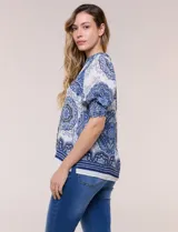 Blusa de crepe color blanco con estampado paisley en tonos azules y negros. Presenta cuello mao con escote en V, cierre frontal con botones y mangas cortas abullonadas con puños elastizados en punto smock.