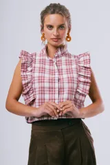 Blusa sin mangas color blanco con cuello alto con volados y detalles de volados en los hombros. Cuenta con cierre frontal de botones.