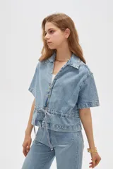 Blusa de jean de manga corta, corte holgado, con cuello en V, cierre frontal con botones y detalles de frunces.