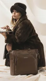 Cartera tipo tote marrón de diseño práctico y versátil, confeccionada en símil cuero con textura granulada. Cuenta con asas cortas fijas, bolsillos exteriores con cierre al frente y atrás, y bolsillos laterales abiertos. Su interior es amplio e incluye bolsillos organizadores. Viene con una correa ajustable y desmontable.