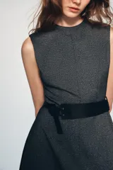 Vestido midi de cuello redondo y sin mangas, confeccionado en tejido jaspeado gris. Presenta un corte evasé y un cinturón ancho de cuero sintético negro con hebilla metálica. Incluye cierre posterior con cremallera oculta.