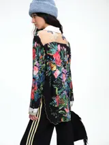 Camisa de corte relajado con estampado floral vibrante sobre fondo negro. Presenta cuello clásico, cierre frontal con botones y puños en contraste. El diseño destaca por sus terminaciones redondeadas y delicadas.