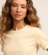 Remera tipo t-shirt de algodón, color beige claro, con cuello redondo y mangas cortas dobladas.