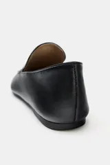 Zapato tipo mocasín de piel negra con copete subido, punta redonda y suela plana.