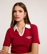 Blusa tipo polo de manga corta, color rojo, con cuello y escote en V con bies blanco contrastante. Presenta una textura gofrada y un bordado pequeño en el pecho con el texto "LE SPORT Paris".