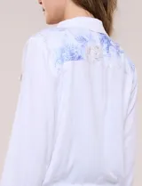 Campera liviana de lino color blanco, con estilo denim y silueta semi entallada. Presenta un canesú superior estampado con motivos florales en tonos azules y tostados, cuello camisero, abotonadura frontal con botones rústicos y bolsillos con solapa en el pecho.