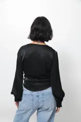 Camisa tipo blusa cruzada de seda negra, con escote en V profundo, mangas largas con puños abotonados y lazo lateral para anudar en la cintura.