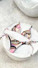 Conjunto de bikini reversible con estampado abstracto multicolor. El top es de estilo triangular con tiras para atar y detalle de argollas metálicas. La bombacha es de corte vedetina, con tiras laterales ajustables y apliques de argollas.