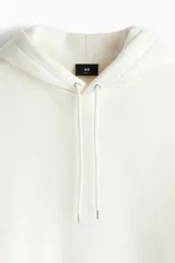 Canguro color crema de corte holgado, con capucha forrada con cordón ajustable, hombros caídos, bolsillo tipo canguro y puños y bajo acanalados.