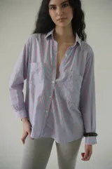 Camisa de rayas verticales rosadas y celestes, con cuello clásico, botonadura frontal y doble bolsillo delantero. Tiene un calce relajado y terminación curva en el ruedo.
