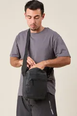 Bandolera negra con correa ajustable, cierre superior y bolsillo frontal con cierre.