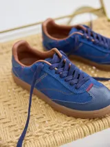 Championes de cuero color tostado con detalles metalizados y pespuntes decorativos en verde y azul. Cuentan con cordones marrones y suela de goma texturizada.