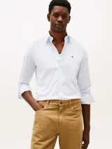 Camisa de corte regular confeccionada en popelín de mezcla de algodones color celeste con microestampado sutil. Presenta cuello camisero, mangas largas con puños abotonados y el logo bordado de Tommy Hilfiger en el pecho.