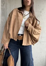 Campera tipo bomber de gamuza con diseño relajado, cierre frontal, cuello camisero y detalles de apliques en los hombros.