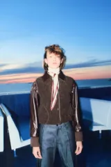 Chaleco de tejido sherpa (borreguito) color marrón oscuro, con cuello redondo y cierre frontal de botones. Presenta ribetes de cinta a tono y bolsillos redondos en la parte delantera.