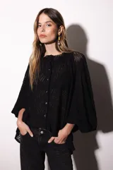 Camisa holgada de popelina de algodón con diseño de rayas verticales en tonos rosado, blanco y negro. Presenta cuello alto con volado, hombros caídos y mangas anchas abullonadas con puños ajustados. Cierre frontal con botones.