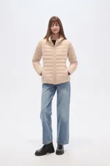 Campera acolchada tipo puffer, color beige claro, con capucha y cierre frontal. Presenta costuras horizontales y un calce entallado.