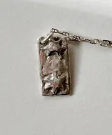Collar amuleto de plata con dije rectangular texturizado que presenta dos estrellas en relieve, acompañado de una cadena de eslabones.