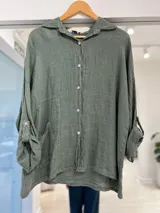 Camisa de lino color verde seco, de corte holgado, mangas largas con presillas para arremangar y bolsillos frontales.