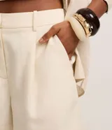 Short femenino color marrón oscuro, con trabillas en la cintura, pliegues frontales y solapa trasera.