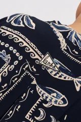 Camisa oversize azul marino con estampado de motivos marinos, palmeras y elementos geométricos en tonos claros. Presenta cuello mao y cierre frontal de botones.
