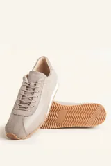 Zapatilla tipo runner color gris claro, de cuero y gamuza combinada, con suela de caucho blanca.