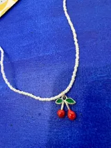 Collar corto tipo choker compuesto por pequeñas cuentas nacaradas blancas, con un dije central en forma de cerezas con hojas verdes esmaltadas.