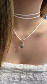 Gargantilla doble de cordón blanco con dije metálico plateado en forma de hoja.